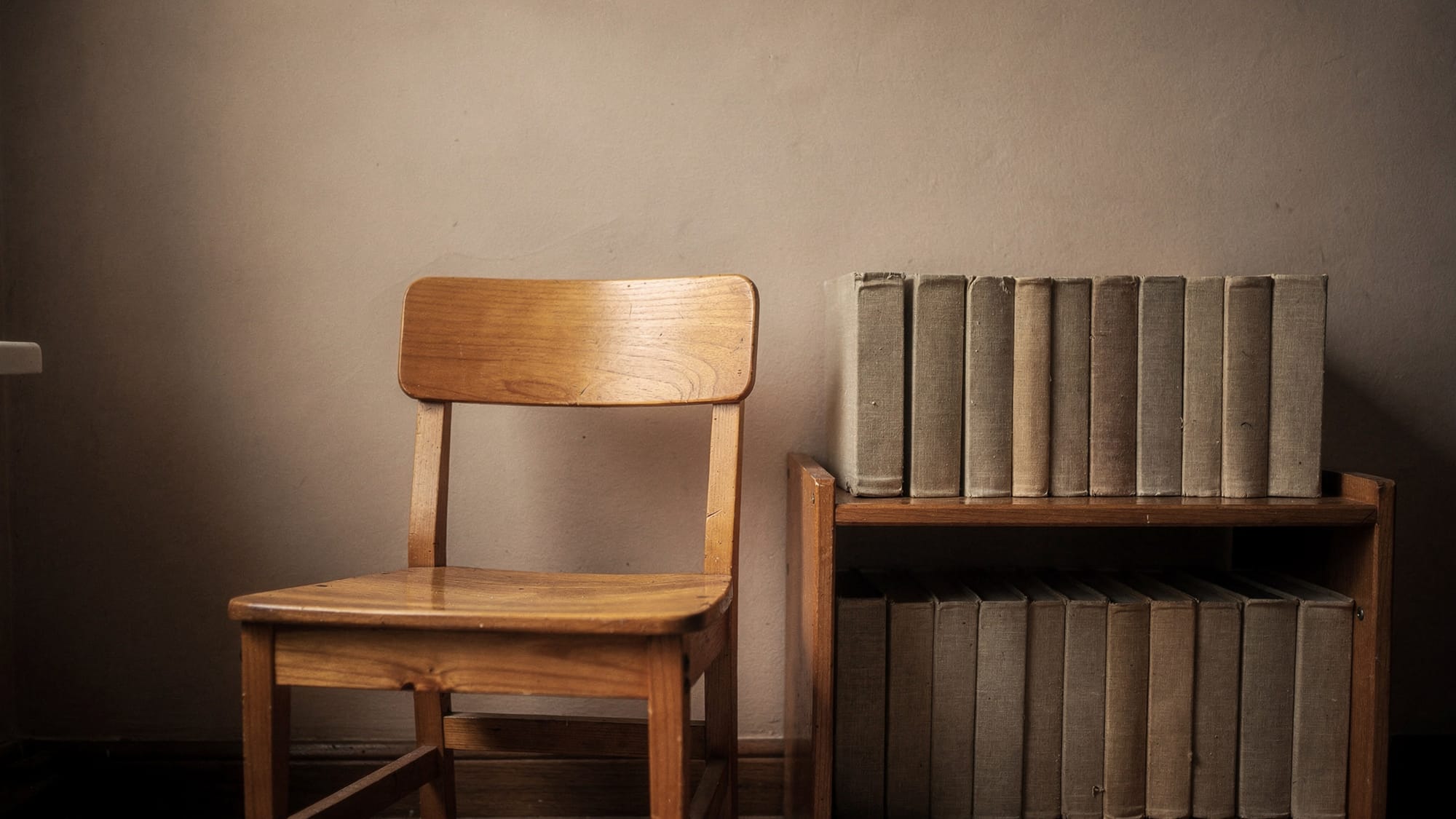 A wooden chair beside a low bookshelf in flat midday light.